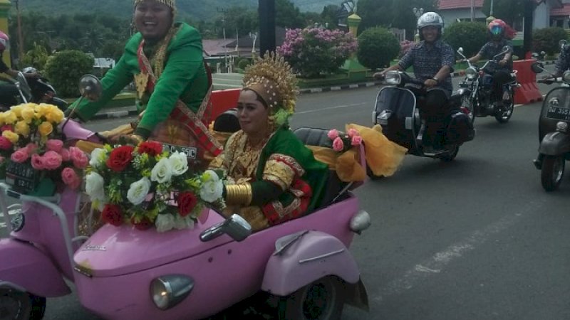 Pasangan Andi Mukramin dan Andi Yuliana tersenyum semringah di atas vespa merah jambu, Minggu (13/1/2019).