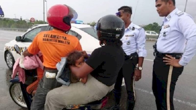 Polisi menghentikan pemotor yang berboncengan empat saat hujan.