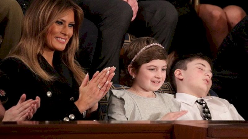 Ibu Negara Amerika Serikat, Melania Trump (kiri), duduk di samping gadir penyintas kanker, Grace Eline, dan Joshua Trump (kanan) yang tampak tertidur dalam agenda pembacaan pidato kenegaraan di US Capitol, Selasa (5/2/2019). 