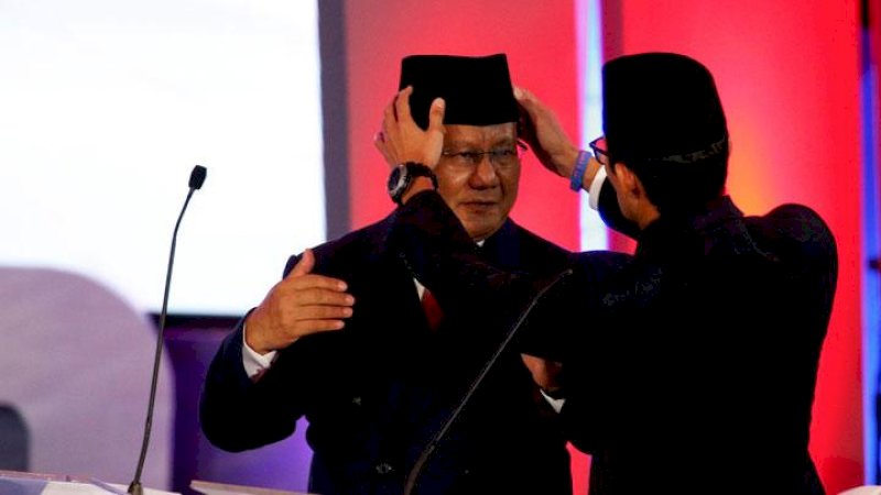 Sandiaga Uno memperbaiki letak kopiah Prabowo di sela-sela debat.