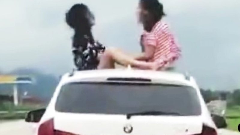 Dua gadis sedang bermain gunting-batu-kertas di atas BMW yang melaju.