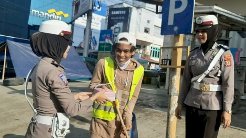 Seorang polwan menyodorkan dus berisi snack ke seorang penyapu jalanan di Wajo.