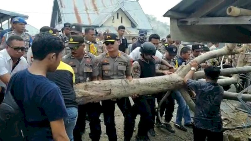 Warga dan polisi,  membuka batang pohon yang dipakai memblokirjalan di Desa Bulusibatang, Jeneponto.