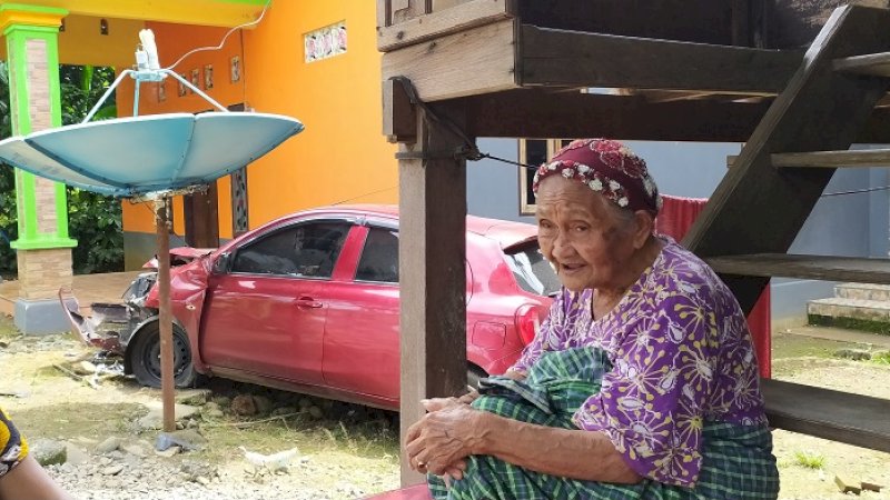 Hajah Sama dengan latar belakang mobil yang mengalami kecelakaan.