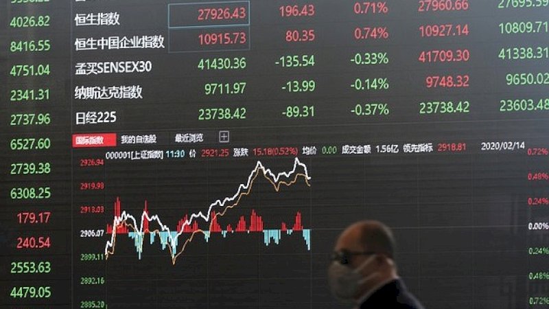 Seorang pria yang mengenakan masker berjalan di depan papan informasi di Shanghai Stock Exchange. (AP)