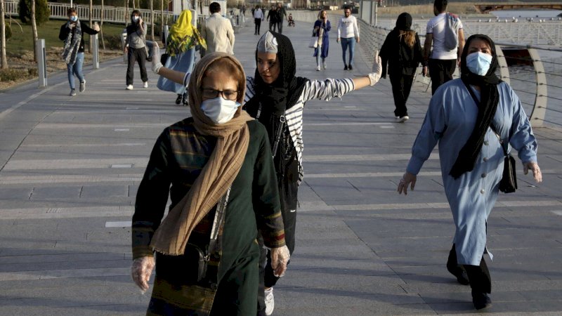 Orang-orang memakai masker di tepi danau buatan, di Teheran Barat, Iran, Minggu, 15 Maret 2020. (AP)

