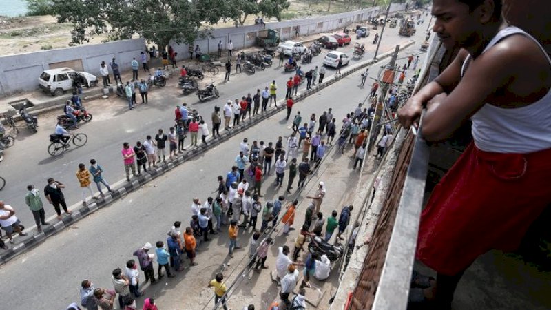 Seorang pria menyaksikan warga yang antre di depan sebuah toko minuman keras di New Delhi. (FOTO: ANI) 