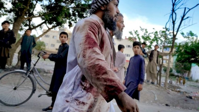 Seorang jemaah yang berlumuran darah berjalan dari masjid tempat ledakan terjadi di Kabul, Afghanistan, Jumat (29/4/2022). (Foto: Ebrahim Noroozi/AP)