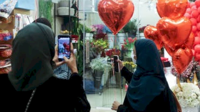 Seorang wanita mengambil foto dengan ponselnya sementara yang lain memegang balon berbentuk hati saat berbelanja di toko bunga menjelang Hari Valentine di Riyadh, Arab Saudi, 13 Februari 2021. (File foto: Reuters)