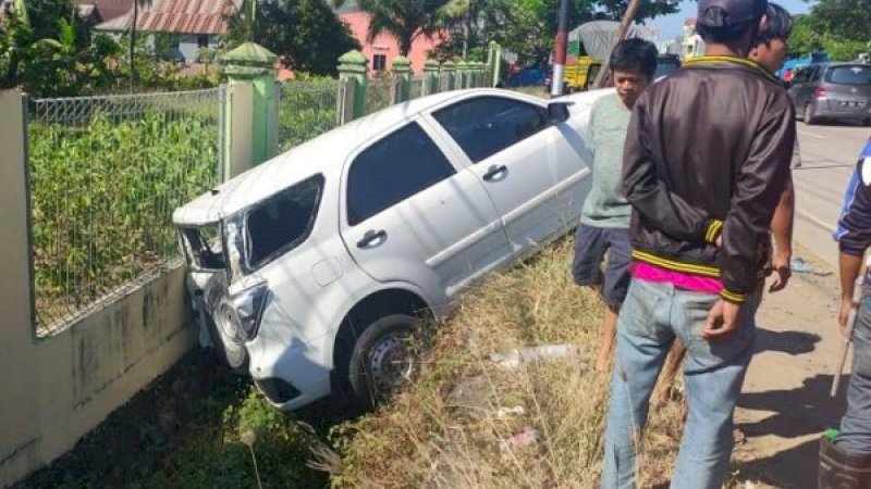 Mobil pelat merah yang dikemudikan terlihat ringsek bagian belakang. Sebagian bodi mobil masuk got.